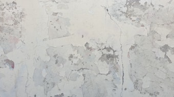 A surface with peeling paint and noticeable cracks. The texture is rough with patches of flaking and discoloration, creating an aged and weathered appearance.