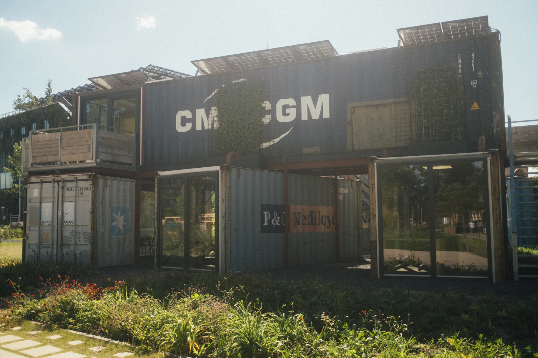 A two-story building made of stacked weathered shipping containers with glass doors cut into the ends