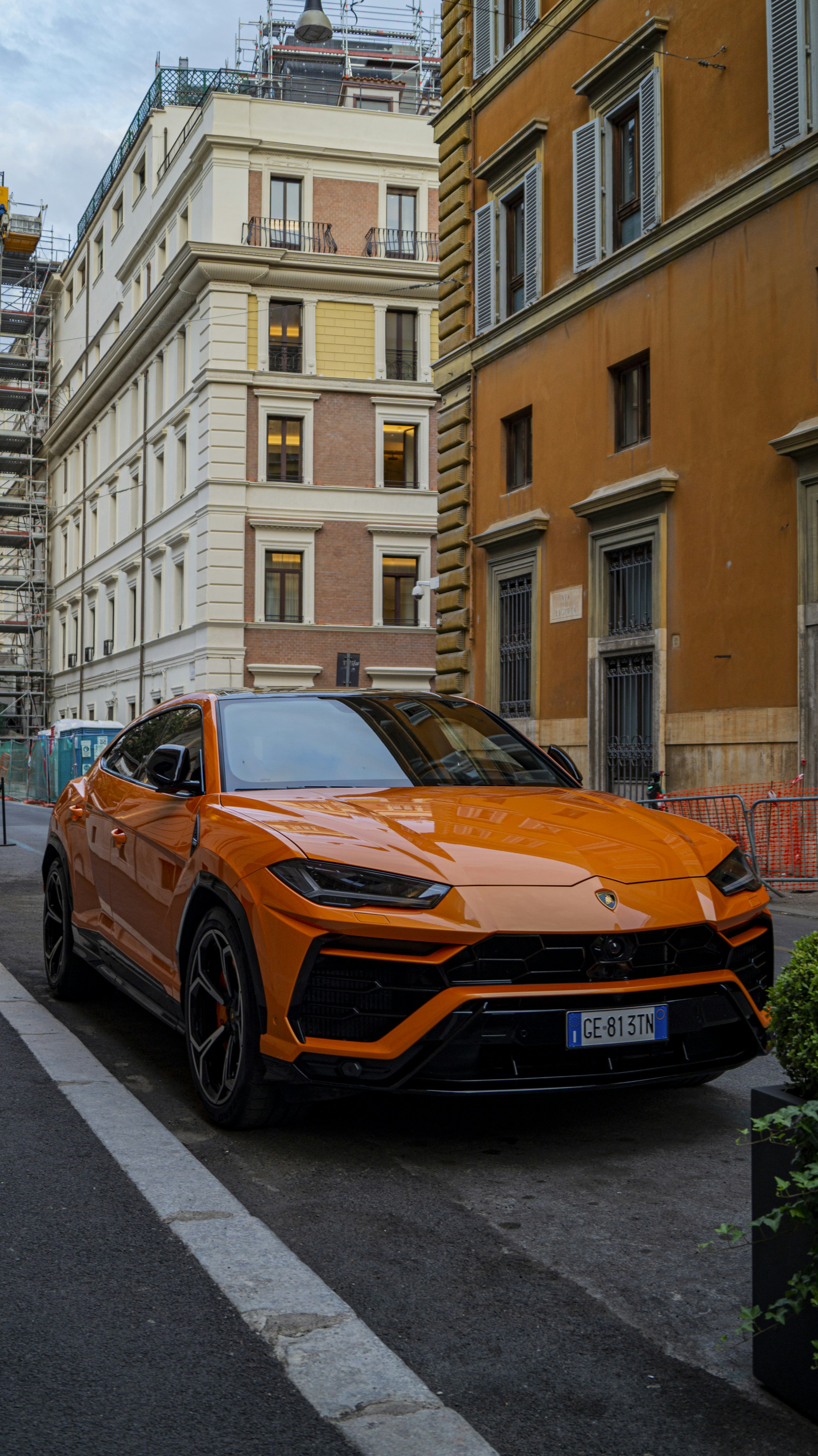 Orange Lamborghini Urus SUV on desert road, dramatic sky, Italian super SUV
