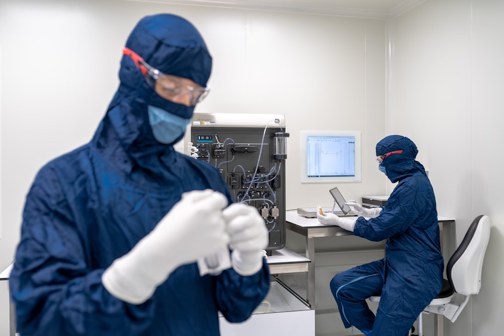 a couple of people in blue protective gear in a room with a computer