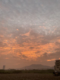 A vibrant sunset behind the Ko'olau mountain range, with a small business storefront lit warmly in the foreground.