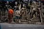 Several people work on large clay sculptures depicting figures from Hindu mythology, with an emphasis on detailed craftsmanship. The scene takes place in an artisan workshop, indicating a cultural and religious context. The figures are at various stages of completion, surrounded by tools and materials.