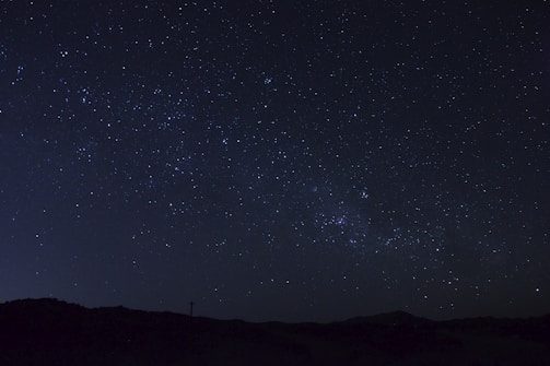 A night sky filled with stars and constellations against a dark horizon