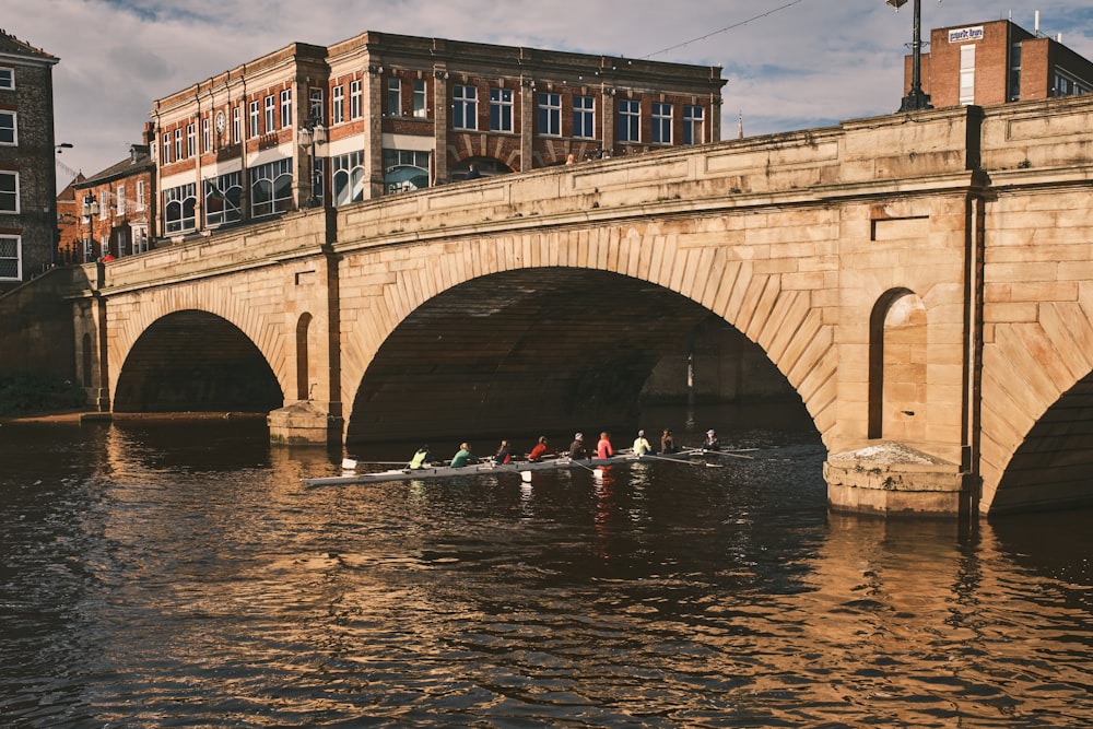 a group of people rowing a boat under a bridge