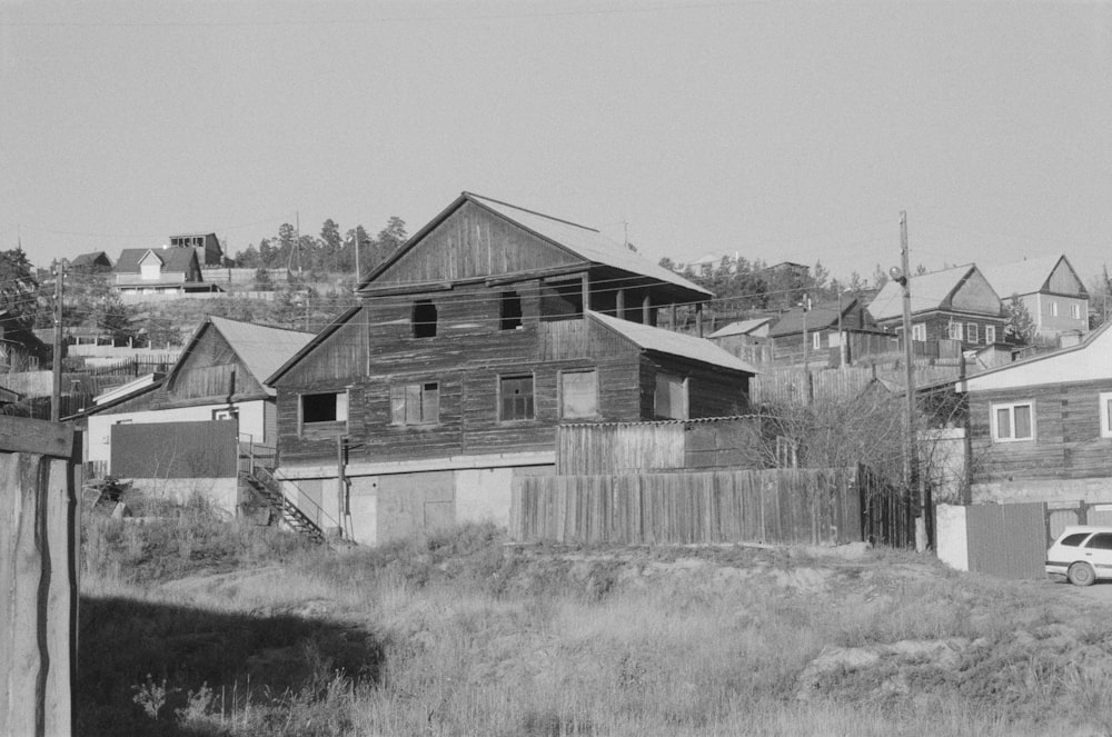 a black and white photo of a house with a fence and a car parked in front