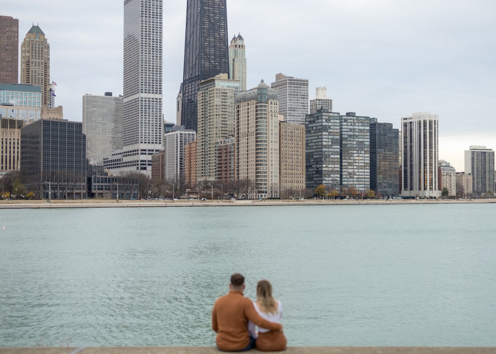 a man and woman sitting on a dock in front of a city