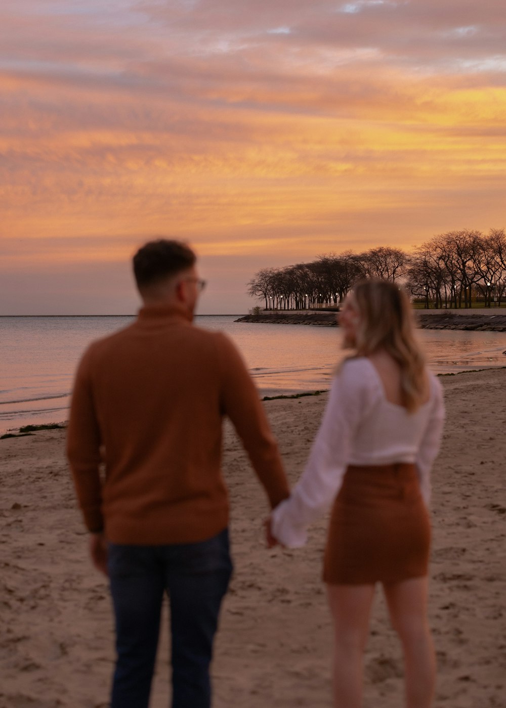 a man and woman standing on a beach at sunset