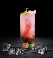 a glass of red liquid with a slice of lemon and a few coins