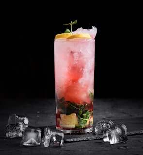a glass of red liquid with a slice of lemon and a few coins