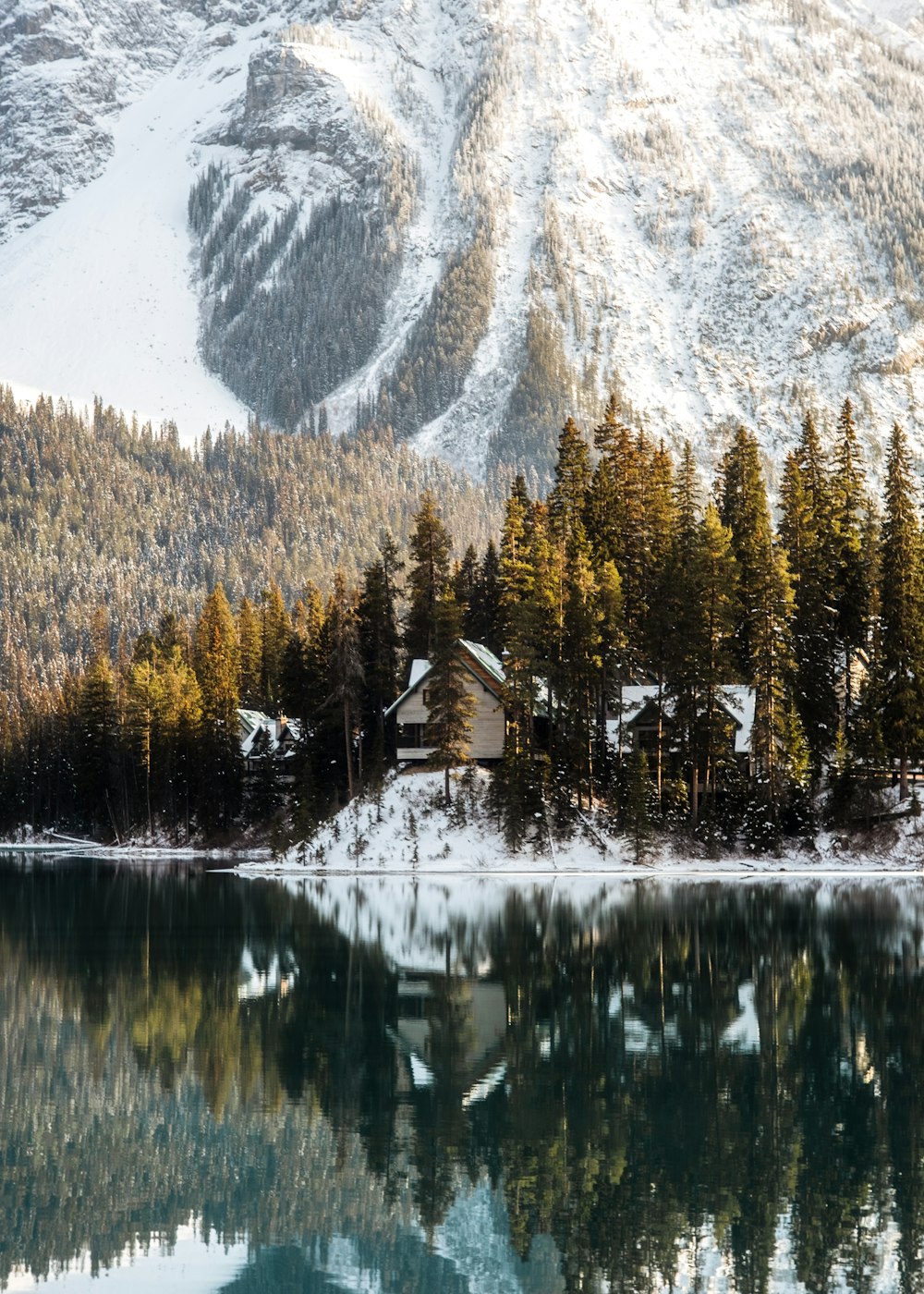 a house by a lake with trees and mountains in the background