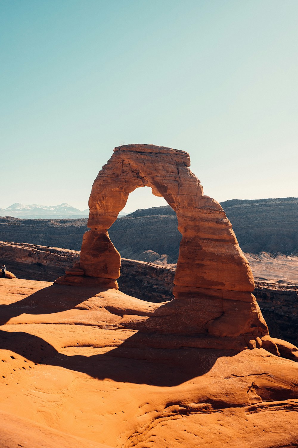 uma grande formação rochosa no deserto com o Parque Nacional dos Arcos ao fundo
