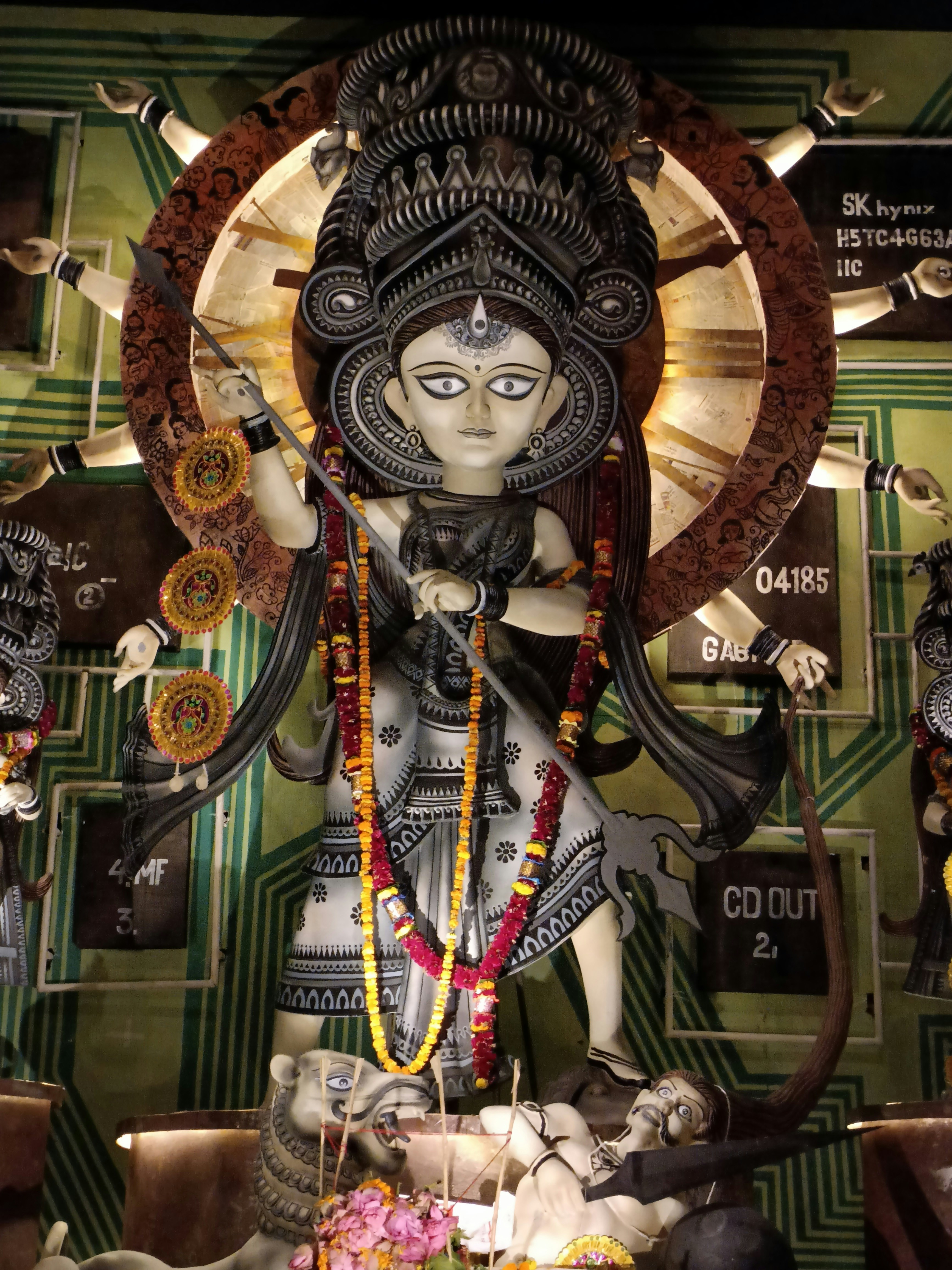 Goddess Durga idol with ten arms holding weapons, surrounded by marigold garlands and diyas
