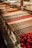 A display case filled with a variety of colorful and neatly arranged pastries or sweets. Each row features different types of confections, including chocolates and round, red truffles. The background includes trays of more pastries, showcasing a rich assortment of treats.