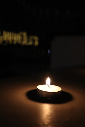 Close-up of a tealight candle softly glowing in a clear holder on a wooden table.