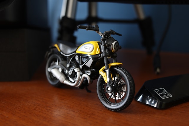 A detailed close-up of a miniature motorcycle model displayed on a wooden shelf.