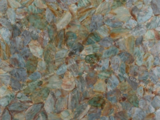 An arrangement of leaf-like gemstones in various shades of green, blue, and brown is spread across the surface, creating an intricate and natural pattern.