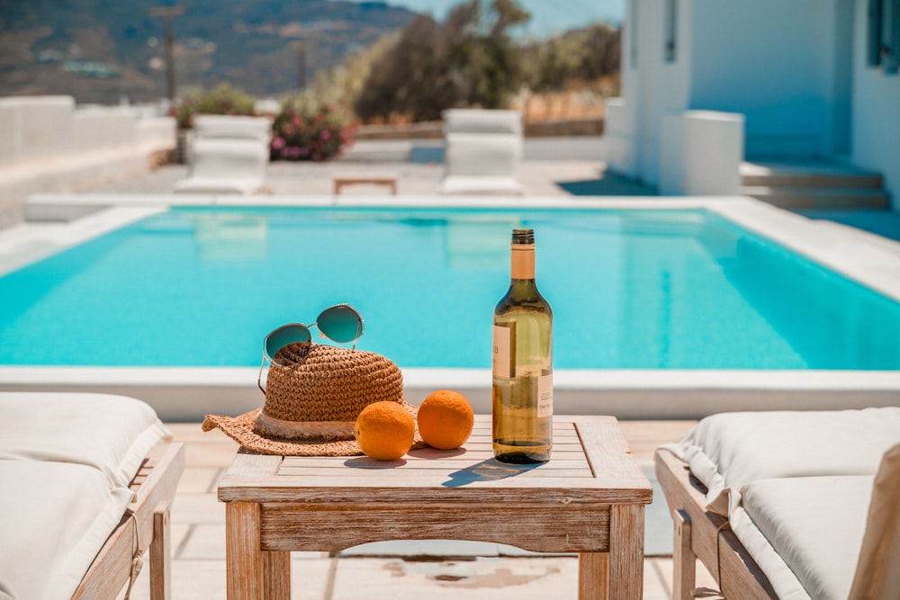 uma mesa com uma garrafa e uma cesta de laranjas à beira de uma piscina