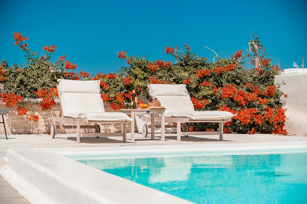 a pool with chairs and a table by it with flowers on the side