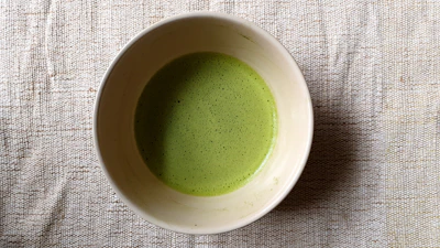 A delicate porcelain bowl filled with vibrant green matcha powder resting on a soft cream linen cloth.