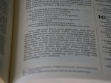 An open book displaying a passage with numbered verses and a significant amount of text in two columns per page. The focus is on a passage that includes phrases about life, knowledge, and enjoyment. The background is slightly blurred, drawing attention to the central text.