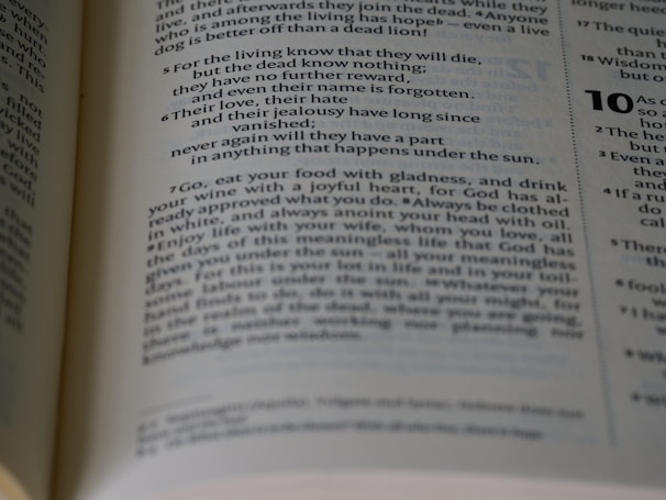 An open book displaying a passage with numbered verses and a significant amount of text in two columns per page. The focus is on a passage that includes phrases about life, knowledge, and enjoyment. The background is slightly blurred, drawing attention to the central text.