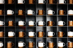 A set of four mugs arranged on a sleek black shelf, each showcasing different bold designs in black, white, and gold accents