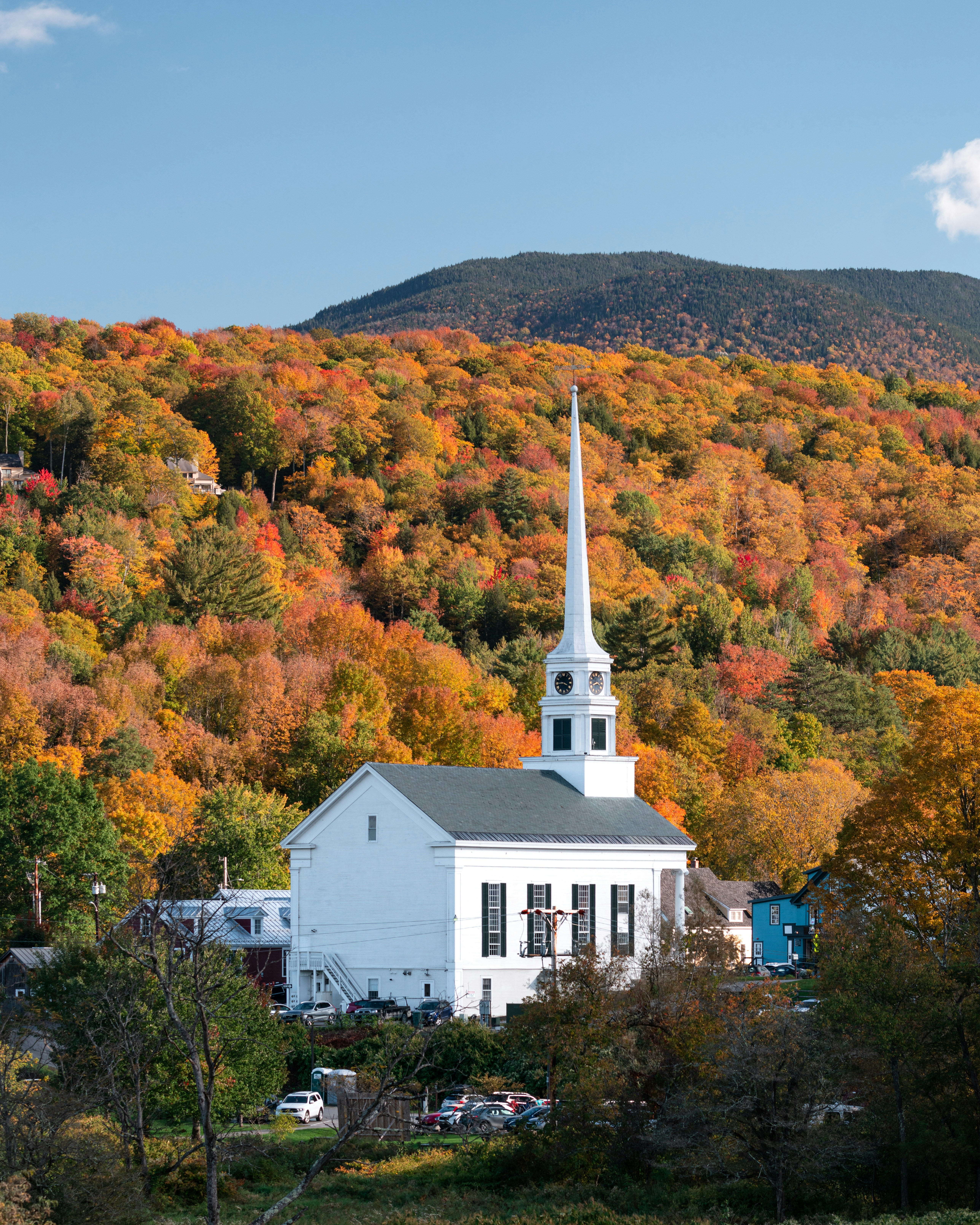 a white building with a steeple surrounded by trees and a hill with orange and yellow leaves