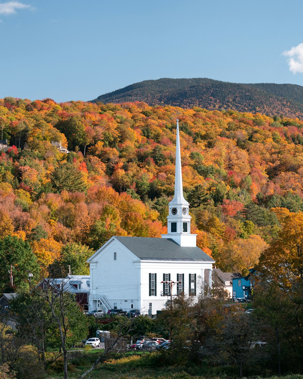 a white building with a steeple surrounded by trees and a hill with orange and yellow leaves