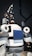 The image features a humanoid robot with mechanical arms and a screen on its chest. The robot has a sleek design with a combination of white, gray, and black colors. It appears to have multiple joints and components, giving it a complex, technical appearance.