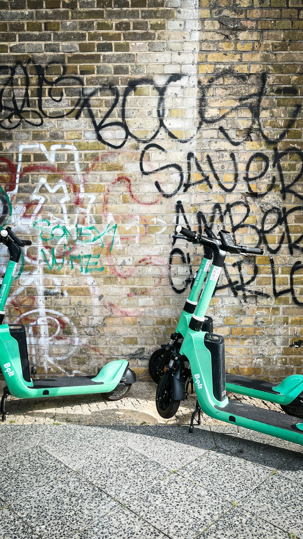 a green scooter parked next to a brick wall with graffiti