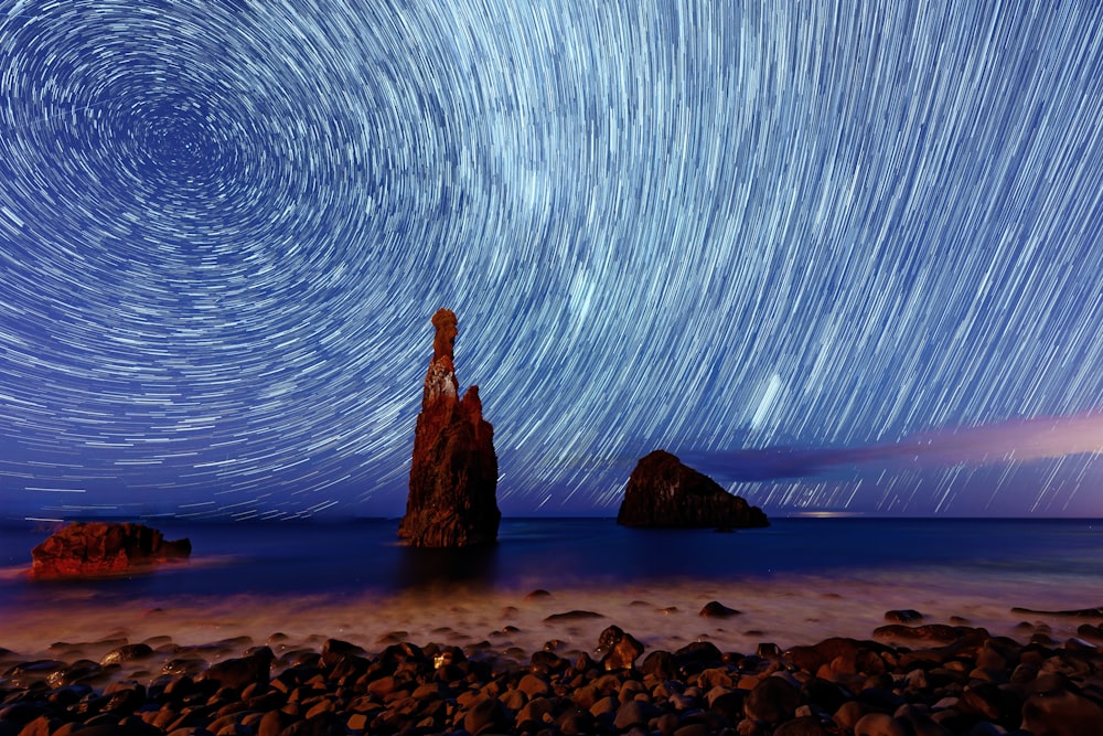 uma praia rochosa com um céu cheio de estrelas acima dela