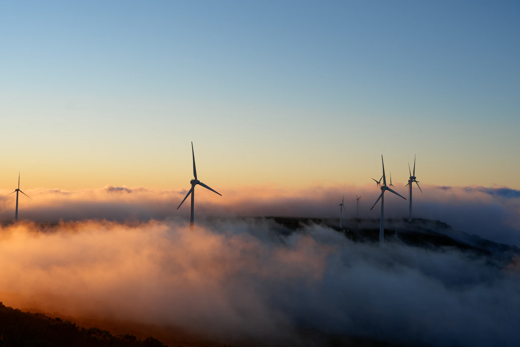 Wind turbines standing above a sea of cloud at sunrise