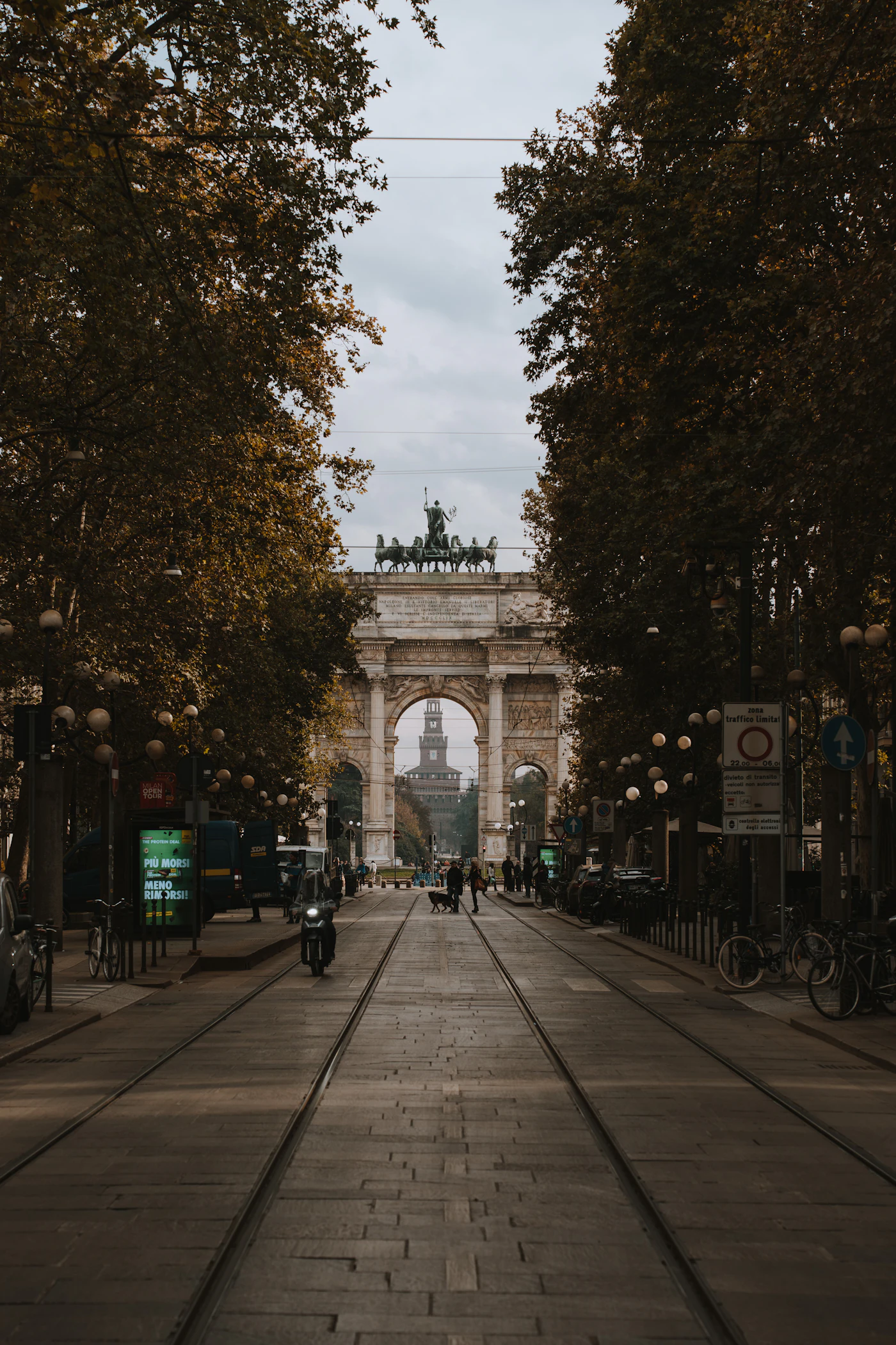 A stone archway opening onto a Milanese courtyard with trees and bicycles