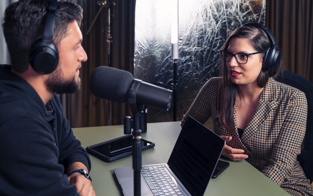 a man and a woman wearing headphones and looking at a laptop