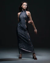 A model posing confidently in a flowing, modern prom dress with a dramatic train against a dark backdrop.