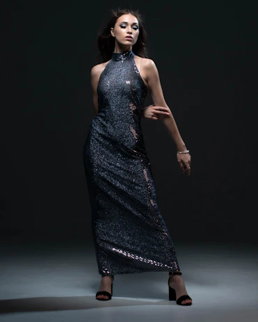 A model posing confidently in a flowing, modern prom dress with a dramatic train against a dark backdrop.