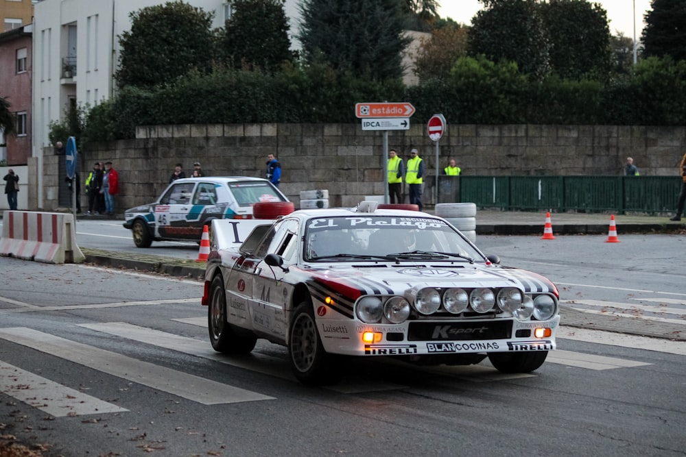 a couple of race cars on a road with people standing around