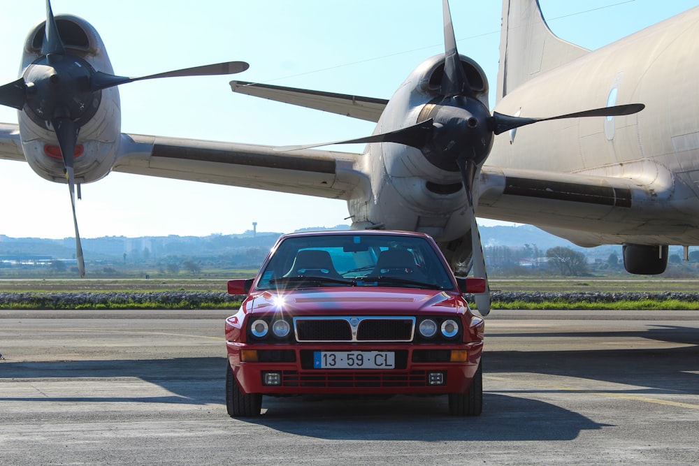 a red car parked in front of a plane