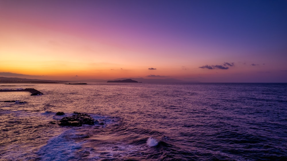 a body of water with rocks and a sunset in the background