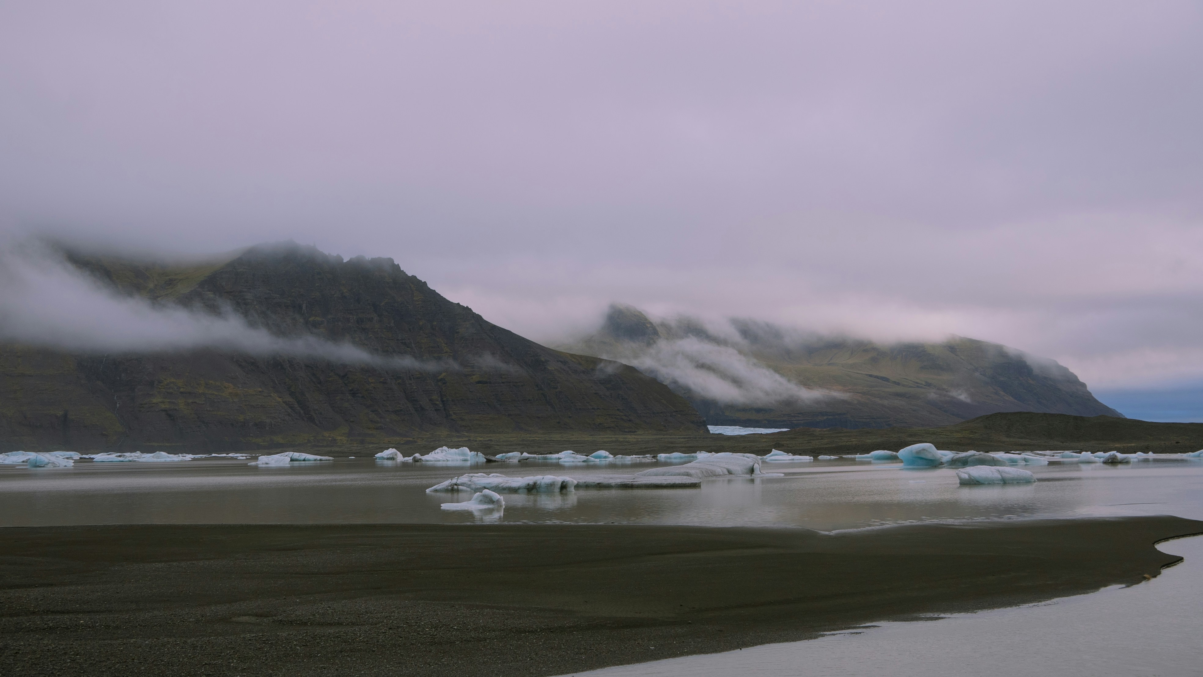 a group of icebergs in the water with mountains in the background