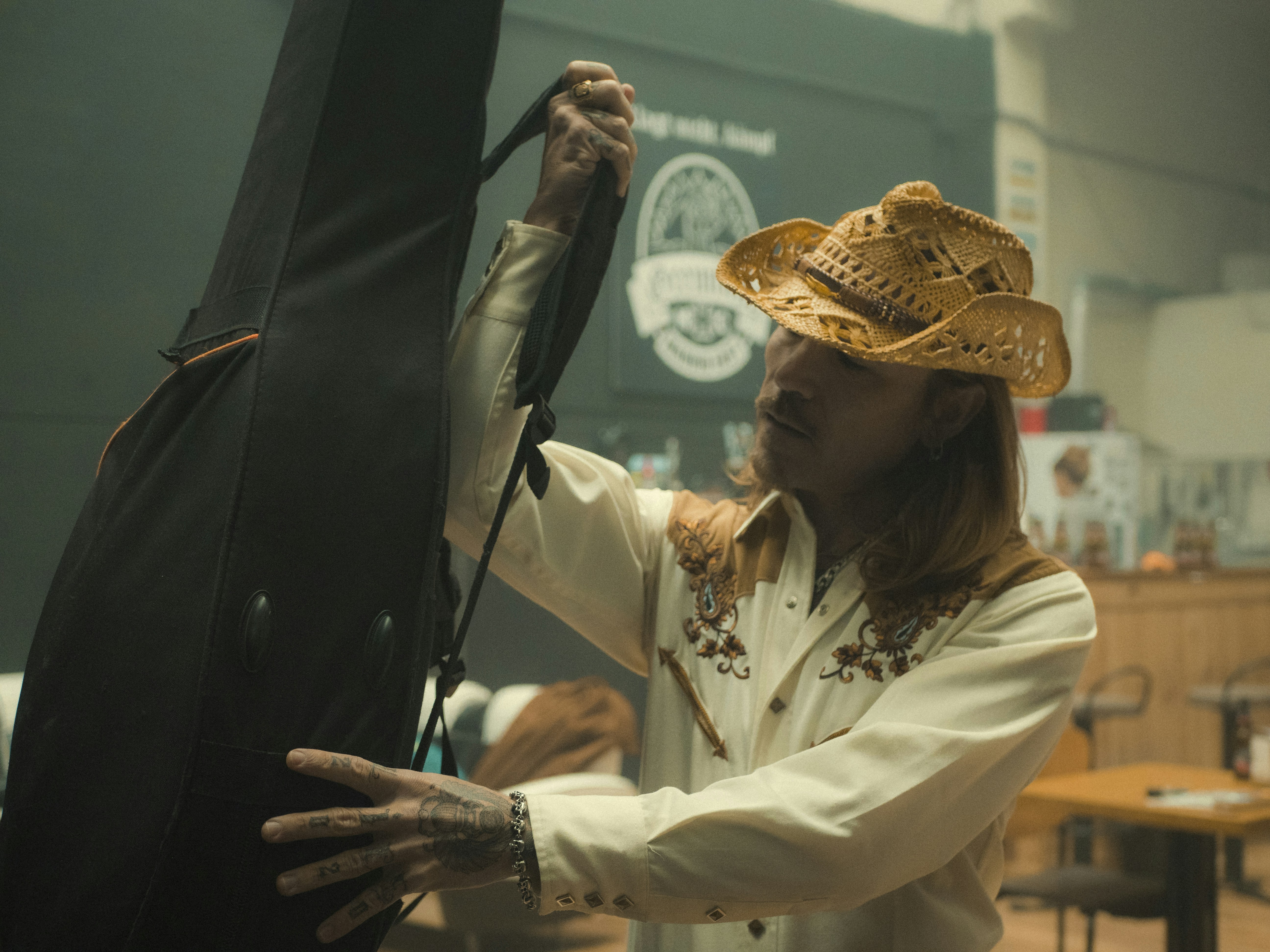 A man in a cowboy hat lifts his guitar bag onto his shoulder, ready to make a royalty free country music instrumental.