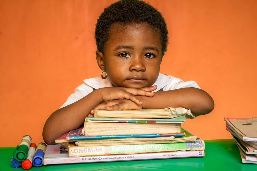 a young girl sitting at a desk with books and a stack of books