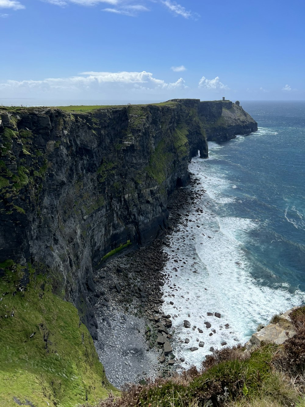 a rocky cliff next to a body of water with Cliffs of Moher in the background
