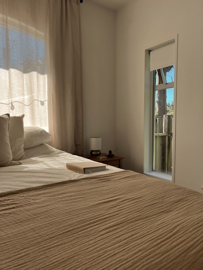 A cozy bedroom softly lit by sunlight filtering through sheer white curtains.