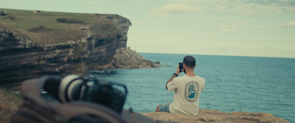 a man sitting on a rock looking out at the ocean