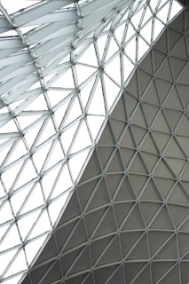 A geometric glass and steel roof structure with triangular panels forming a lattice pattern. The design creates a modern and intricate architectural element.