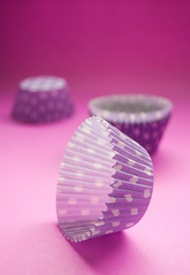 Purple polka-dotted cupcake liners are arranged on a vibrant pink background. One liner is in the foreground, with two others blurred in the distance.