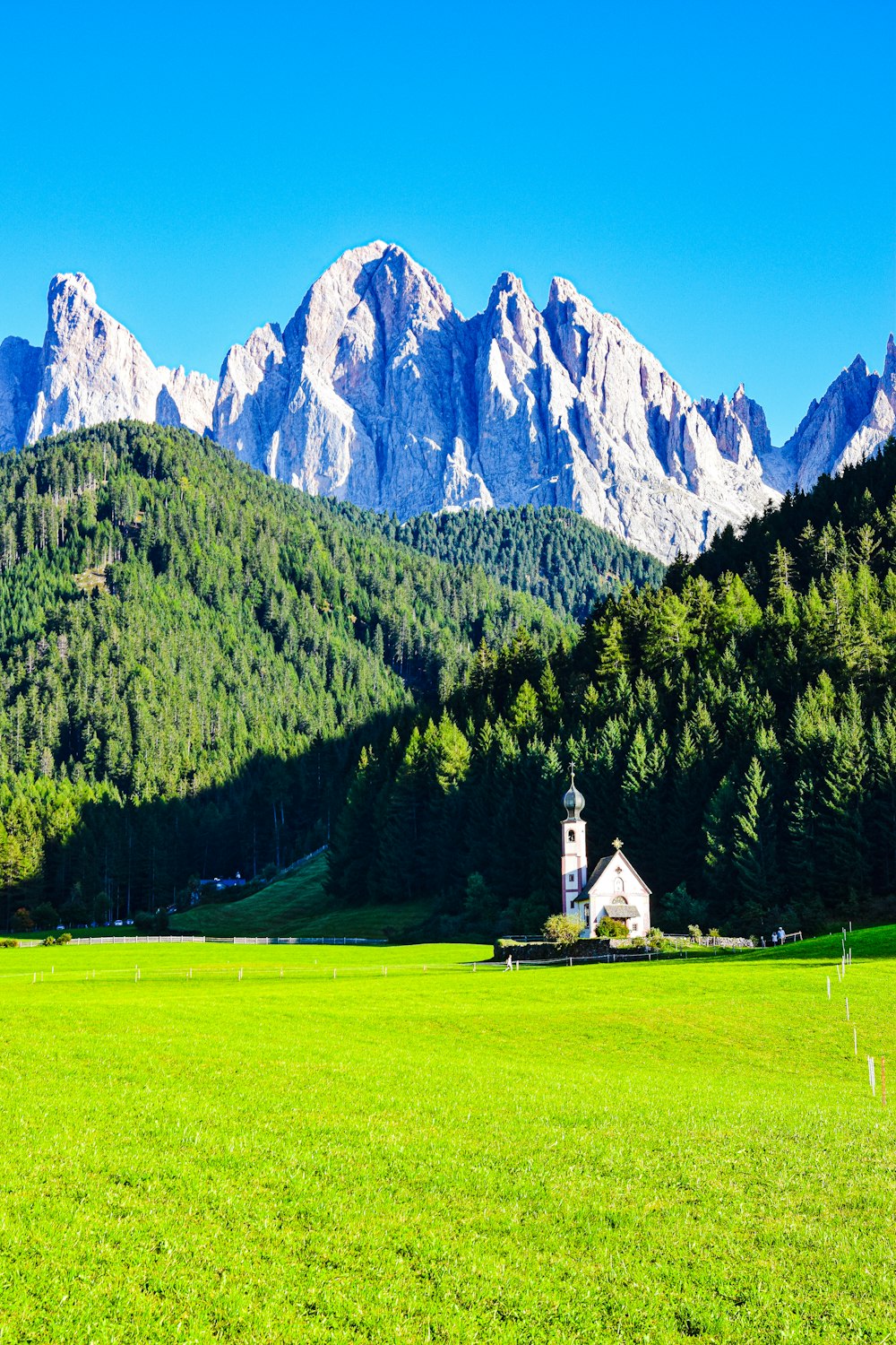 a small white building in a grassy field with mountains in the background