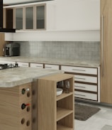 A modern kitchen interior featuring wooden cabinetry and a marble countertop. The kitchen includes a stovetop, a coffee machine, a wine rack with bottles, and open shelving holding wine glasses and a bowl. The backsplash is tiled, and a small rug is placed on the floor.
