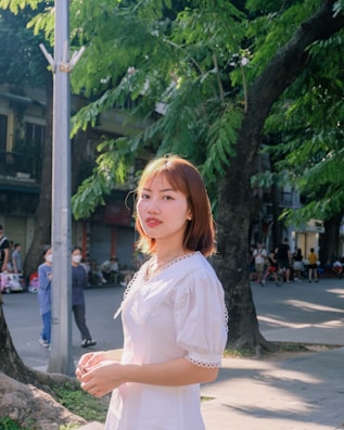 A cheerful young woman wearing a vintage floral dress in a sunlit urban street.